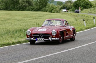 A red Mercedes classic car drives along a picturesque country road surrounded by trees, classic