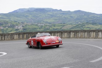 Red open-top sports car on a winding track in a picturesque mountain landscape, Mille Miglia 2014