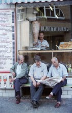 Berlin, DEU, 10.06.1998 -- Turkish men sit reading newspapers in front of a kebab shop. (Free time,