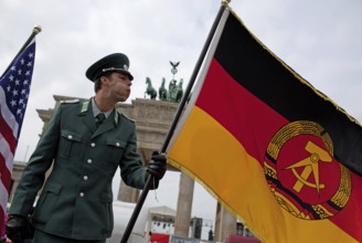 DEU Germany Berlin Actor wearing NVA uniform blows the GDR flag. Scene on the eve of the 20th