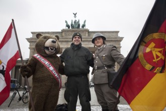 A riot police officer with the Berlin Bear and an actor in NVA uniform is photographed by a