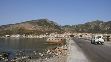 An off-road vehicle on a coastal road with a view of a city and mountains, Monemvasia, Monemvassia,