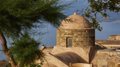Soft morning light, view over a dome and the sea, framed by green trees and tiled roofs,