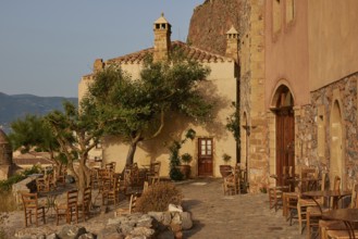 Soft morning light, a rustic outdoor café with tables and chairs on paved ground, sheltered by