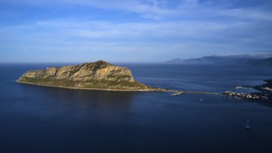 Drone shot, island in the sea, connected by bridge, mountains and sky in the background,