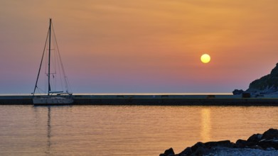 Sailing boat against orange sky and calm sea at sunrise, Monemvasia, Monemvassia, Malvasy,
