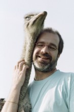 DEU, Mannheim, 22.07.1994 -- ostrich breeder (man, hug, bird ostrich, stroking, affection) -- Â©