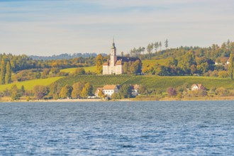 A church on a hill above autumn vineyards and a lake, surrounded by picturesque landscapes and