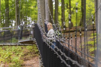 Woman on swinging rope bridge in lush forest, Treewalk, Affenberg Salem, Bodenseekreis, Germany