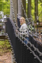 Woman on a rope bridge through a forest, Treewalk, Affenberg Salem, Bodenseekreis, Germany