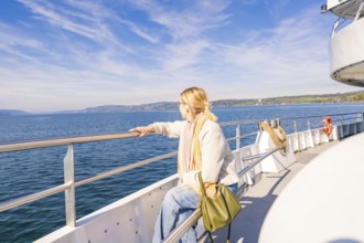 A woman stands relaxed at the railing of a ship and looks out to sea in sunny weather, Schiff