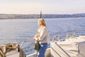 Woman leaning calmly on the railing with a view of the vast water landscape, boat trip, Lake