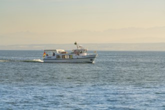 Small white boat with people sailing on a calm lake in sunlight, boat trip, Lake Constance, Germany