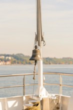 Bell on a ship deck with a view of a sunny coastal landscape, boat trip, Lake Constance, Germany