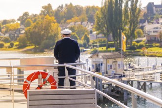 Captain on a ship with a view of the autumnal seaside town, boat trip, Lake Constance, Germany