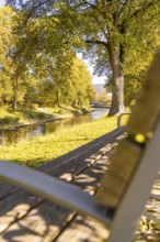Wooden bench overlooking a river in an autumn park, sunbeams through the trees, Nagold, Black