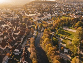 An autumnal view of the city with a river and lots of colorful trees illuminated by the sun,