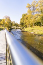 A river flows under a bridge, surrounded by autumn-colored trees on a sunny day, Nagold, Black