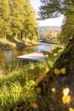 View across the river onto a jetty, captured in golden autumn light, Nagold, Black Forest, Germany