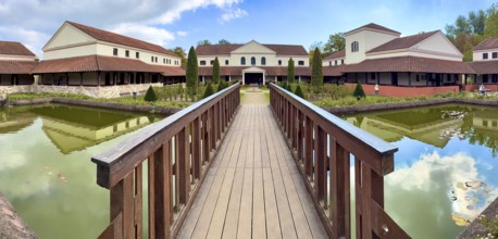 View from site of archaeological open-air museum across small wooden bridge across ornamental pond