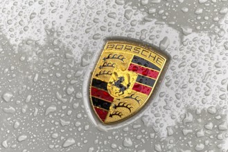 Coloured Porsche crest on sports car bonnet with sparkling raindrops, international