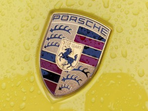 Colored Porsche crest on yellow sports car bonnet with sparkling raindrops, international