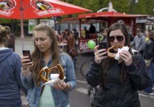 GERMANY Young woman are filming a rally with their mobile phones while eating pretzels. Germany