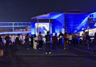 Passers-by watch the projection To the German People — A Parliamentary Search for Clues at the