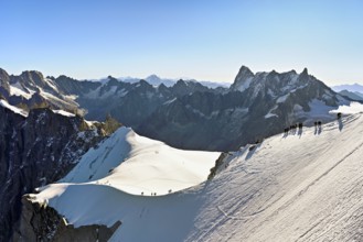 Mountaineers climb over a snow-covered ridge, behind Grandes Jorasses, Aiguille du Midi mountain