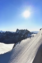 Mountaineers climb over a snow-covered ridge, behind Grandes Jorasses, Aiguille du Midi mountain