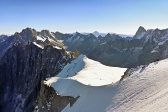 Mountaineers climb over a snow-covered ridge, behind Aiguille Verte, Les Droites, Les Courtes,
