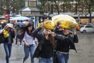 DEU Germany Germany Berlin Young woman walk through the rain, their shopping bags as protection
