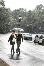 DEU Germany Germany Berlin A couple walking with an umbrella through a summer rain shower at the