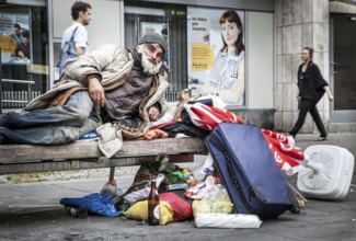 DEU Germany Germany Berlin A homeless person sits on a bench next to his belongings in a square in