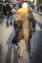 DEU Germany Germany Berlin A woman wears a leopard cloak while using crutches on the Kudamm to pass