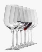 Some wine glasses standing consecutive in a row in white back, one partly filled with red wine