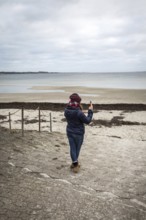 DEU Germany Germany Flensburg A woman takes a photo with her mobile phone on the beach at Holnis