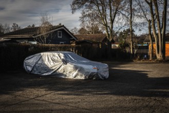 DEU Germany Germany Berlin A car, wrapped in a tarpaulin, is parked in a car park next to an