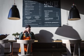DEU Germany Germany Berlin A man eats a sandwich in a snack bar attached to the Rewe supermarket in