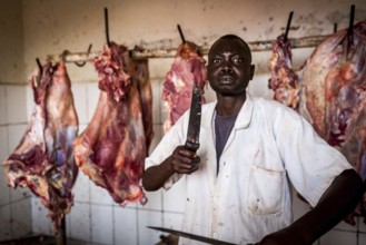 RWA RWANDA Rwanda Kayonza A butcher sharpens his knives in front of pieces of meat. He poses for
