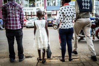 RWA RWANDA RUANDA Kigali A young girl with a white dress and handbag waits with others until she