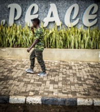 RWA RWANDA RUANDA Kigali A man in camouflage fashion passes a Peace font in the Kiyovu banking