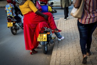 RWA RWANDA RUANDA Kigali A woman in a red skirt gets into a motorbike taxi