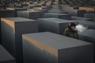 DEU Germany Germany Berlin The Holocaust Memorial as the sun sets. Visitor vaping with an