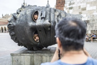 POL Poland Poland Krakow Krakow Asian tourist photographs his children in a sculpture on the Market