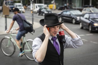 DEU Germany Germany Berlin A man protects his hat from a gust of wind while talking on the phone