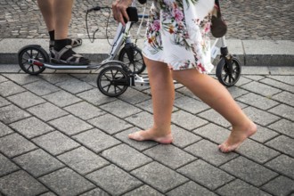 DEU Germany Germany Berlin A woman passes a family on pedal scooters barefoot on Pariser Platz in