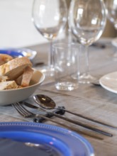 Dining table set with bread, cutlery, blue plate, and wine glasses, ready for a meal
