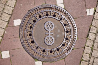 Manhole cover, city coat of arms, sidewalk made of concrete paving stones and paving stones with