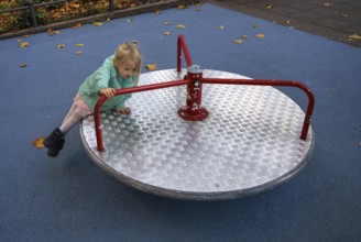 Outdoor shot, little girl, child, 4 years, blonde, playing on carousel, children's playground,